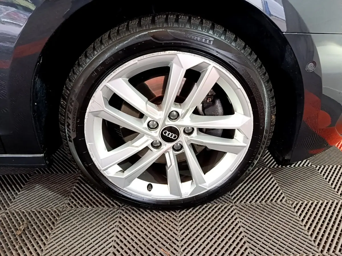 Gros plan sur la roue avant droite d'une Audi A3 gris foncé, avec jante alliage et logo Audi au centre.