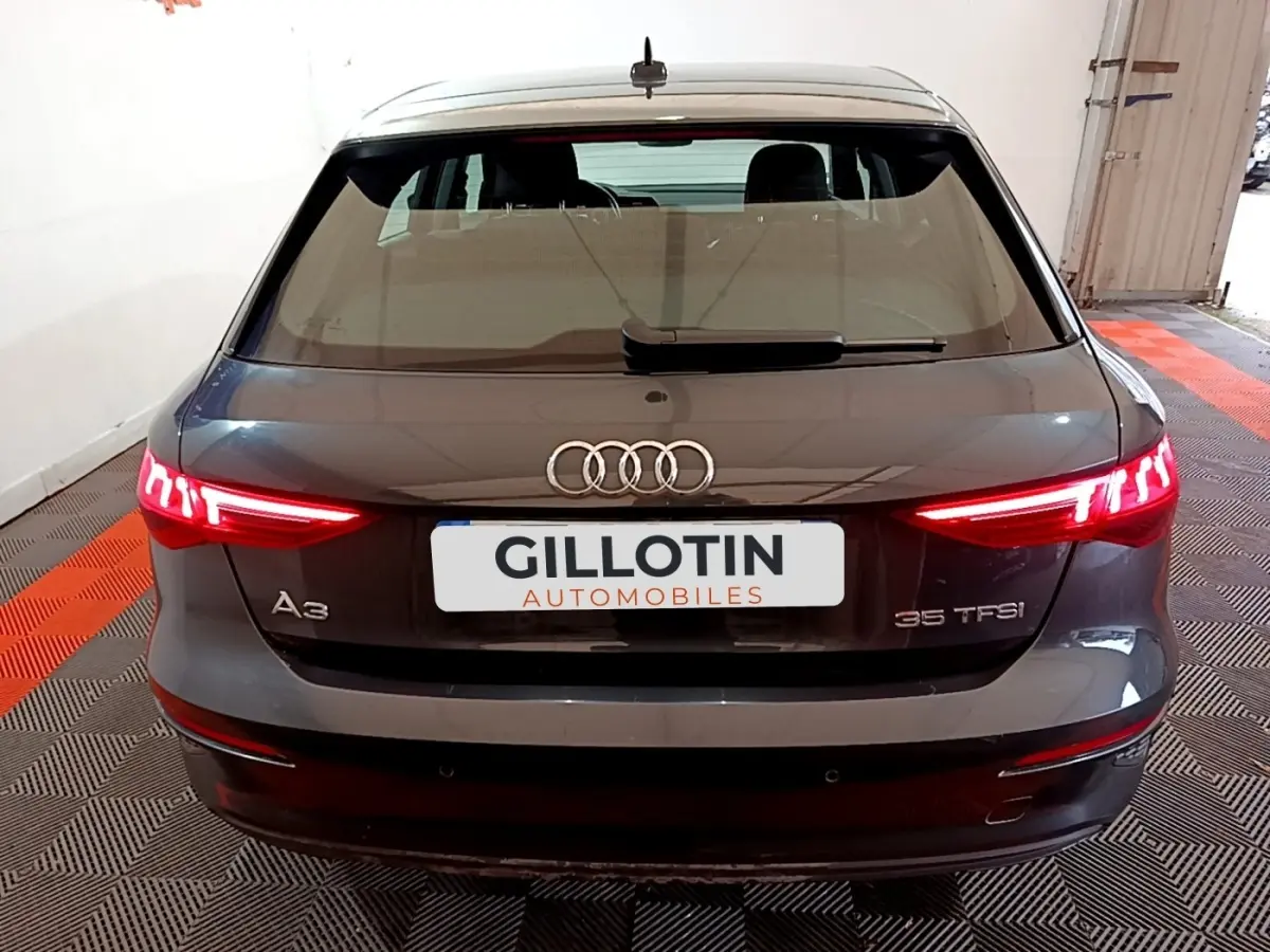 Vue arrière d'une Audi A3 35 TFSI gris foncé avec feux allumés dans un garage fermé.