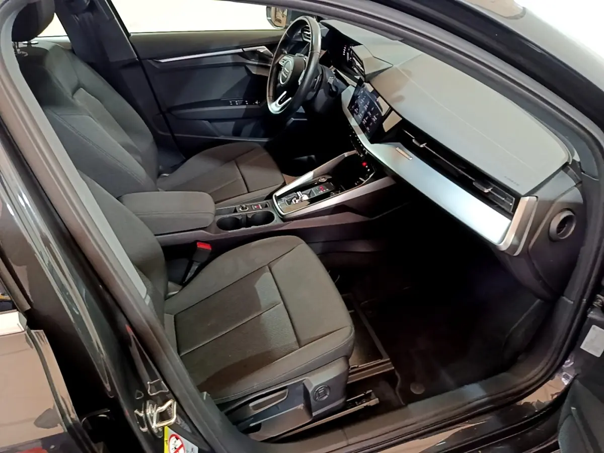 Vue intérieure côté conducteur de l'Audi A3 gris foncé, mettant en valeur le volant cuir multifonctions et le tableau de bord digital.