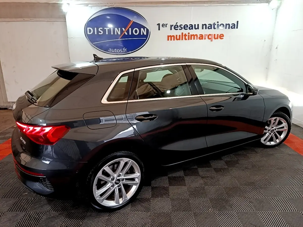 Audi A3 35 TFSI gris foncé vue 3/4 arrière droit, jantes alliage et feux arrière LED allumés.