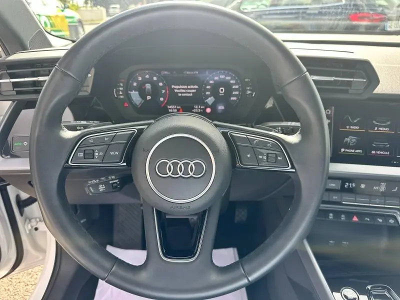 Vue rapprochée du volant cuir multifonction noir d’une Audi A3 Sportback 2024 avec tableau de bord numérique et écran central.