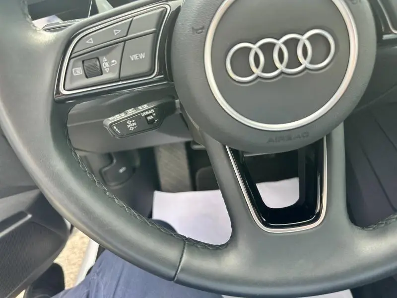 Gros plan sur le volant cuir noir de l'Audi A3 Sportback 2024 avec commandes multifonctions et logo Audi central argenté.