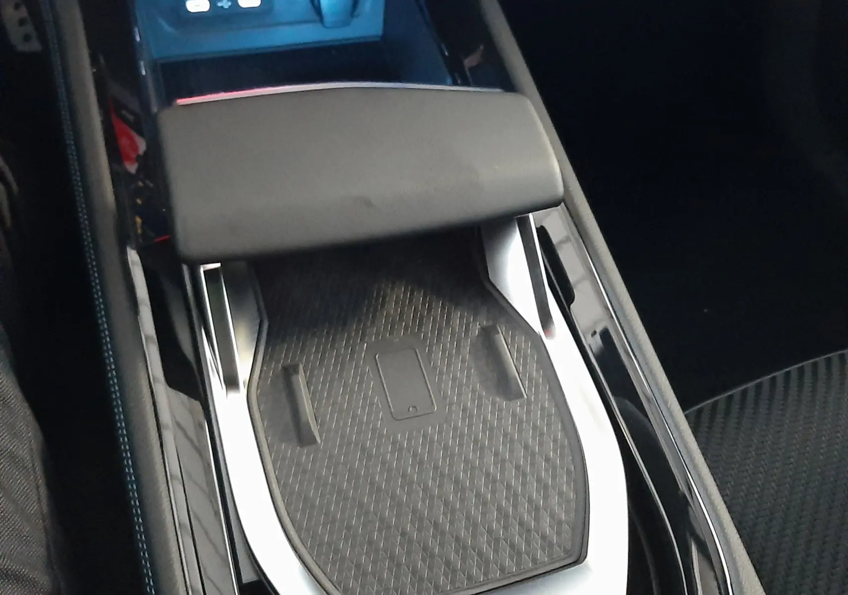 Gros plan sur la console centrale noire du Renault Austral 2025 avec surface de recharge sans fil et accoudoir.