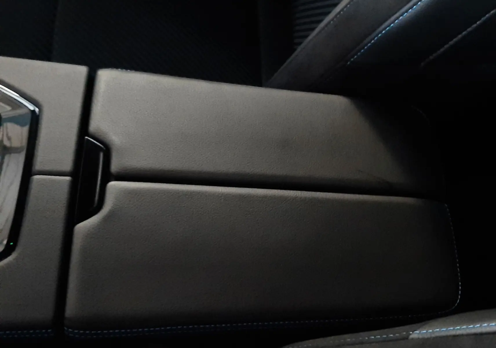 Vue rapprochée de l'accoudoir central noir avec surpiqûres bleues à l'intérieur du Renault Austral E-Tech Hybrid 2025.