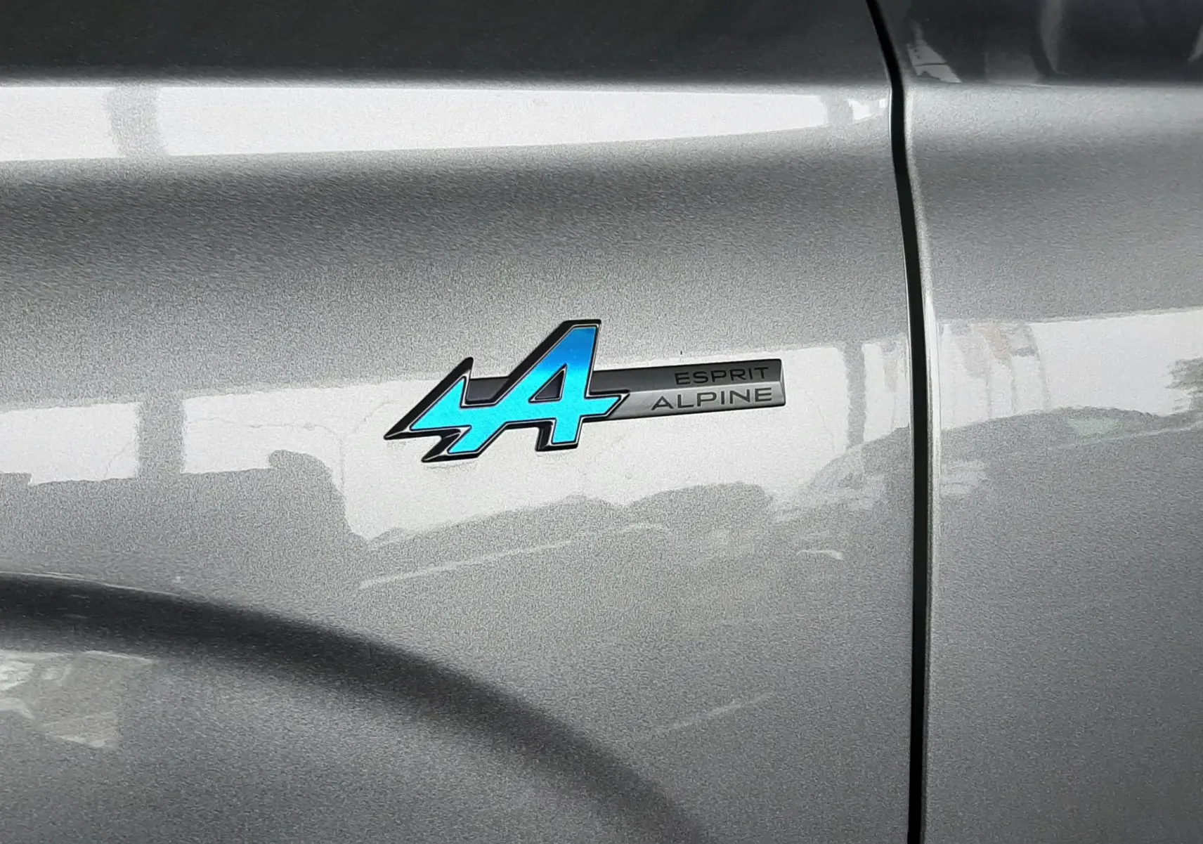 Gros plan sur l’écusson bleu "Esprit Alpine" sur la porte gris schiste satin du Renault Austral 2025.