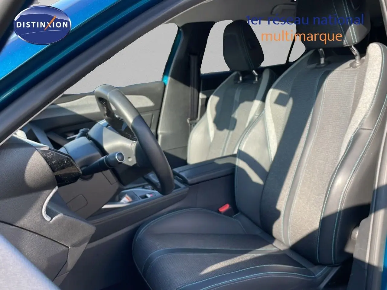 Vue intérieure côté conducteur de la Peugeot 308 2024, sièges tissu et cuir gris noir avec surpiqûres bleues.