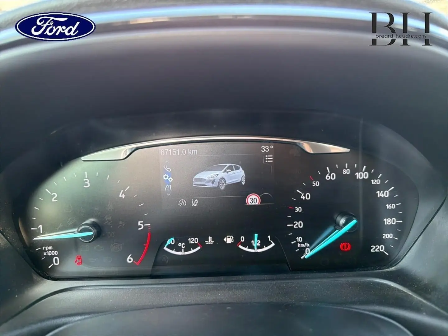 Vue rapprochée du tableau de bord digital de la Ford Fiesta blanc glacier, affichant compteur et écran multifonction.