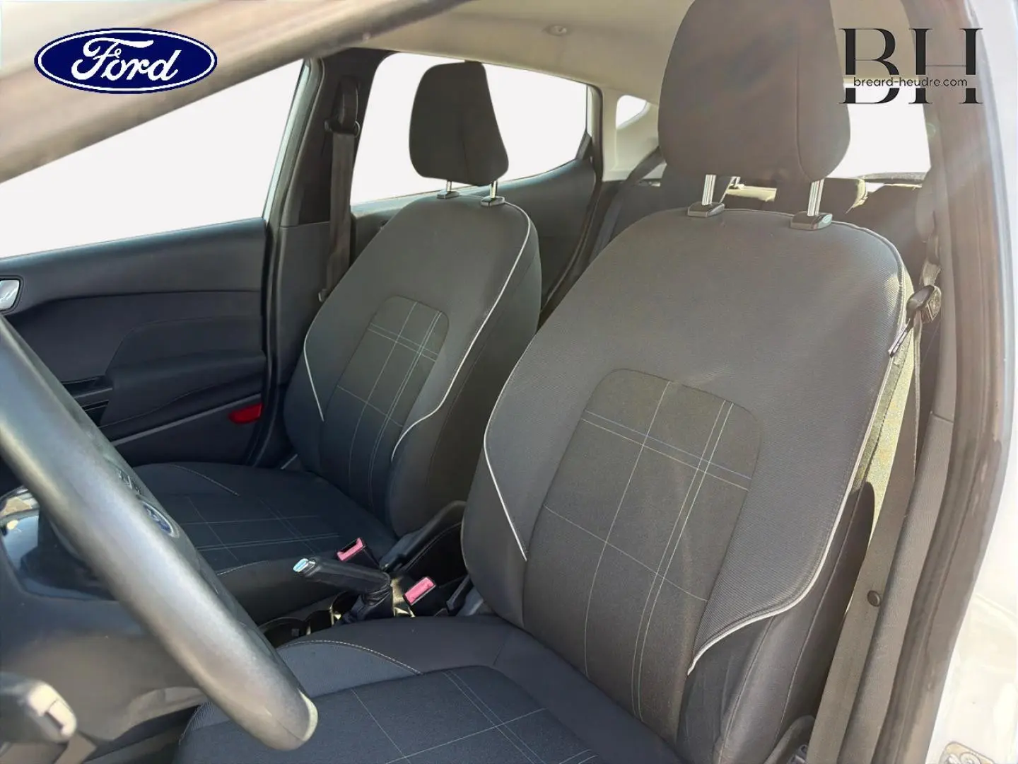 Vue intérieure côté conducteur de la Ford Fiesta 2018, montrant les sièges en tissu noir à motifs gris et la console centrale.
