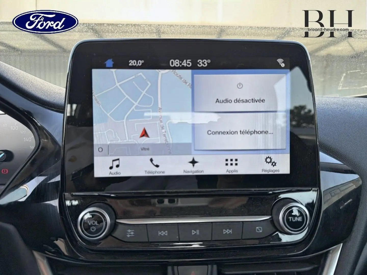 Écran tactile central du tableau de bord de la Ford Fiesta blanc glacier, affichant la navigation et les commandes audio.