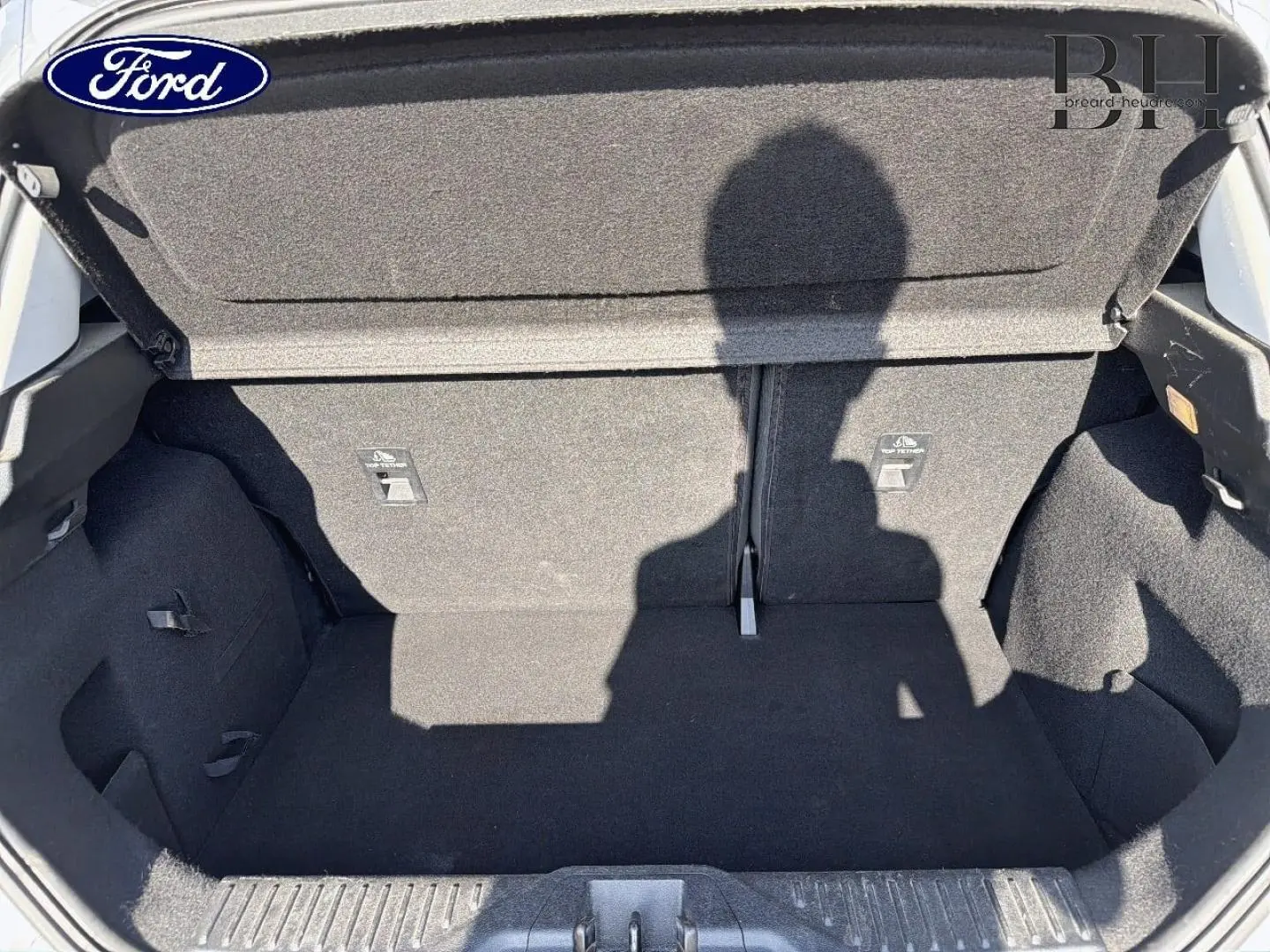 Coffre ouvert de la Ford Fiesta blanc glacier, vue de l'intérieur montrant l'espace de chargement et la banquette arrière rabattable.