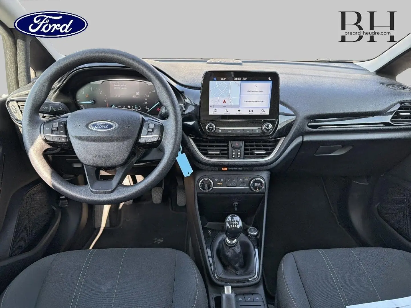 Vue intérieure frontale du tableau de bord et volant noir de la Ford Fiesta 2018 avec écran tactile et levier de vitesses manuel.