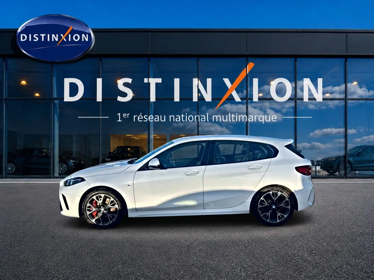 BMW Série 1 blanc alpin vue de profil côté gauche, avec jantes 18 pouces bicolores et étriers rouges visibles.
