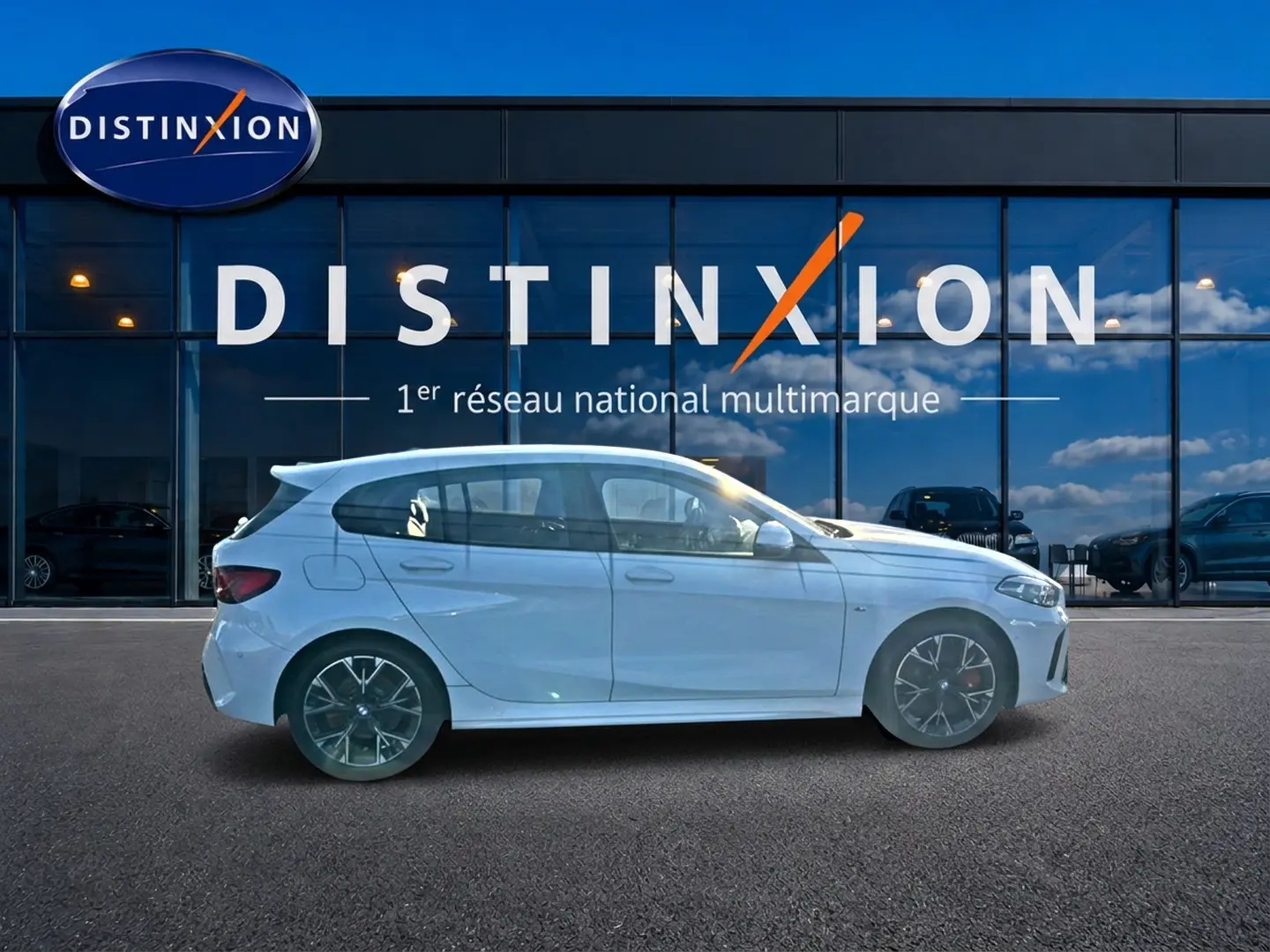 BMW Série 1 blanc alpin vue de profil côté gauche avec jantes 18 pouces bicolores devant une vitrine Distinxion.