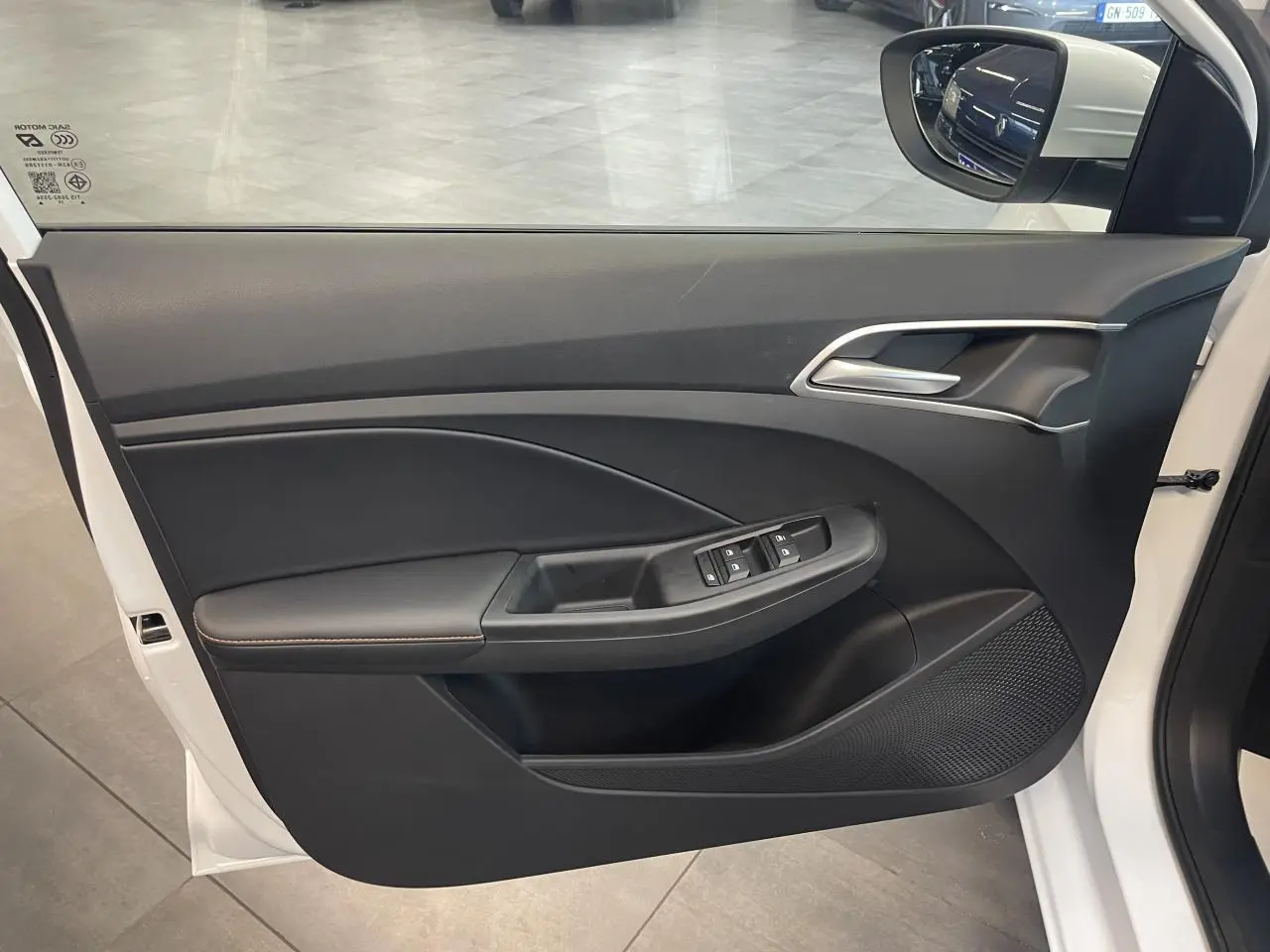 Vue intérieure côté gauche de la porte avant blanche du MG3 1.5 Hybrid+ avec commandes de vitres et poignée argentée.
