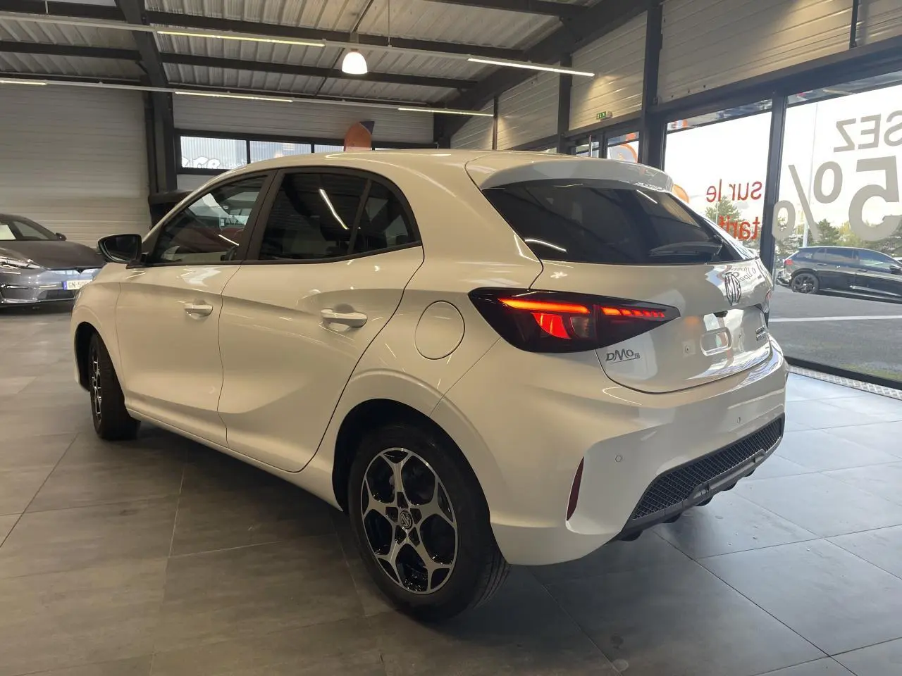 Vue 3/4 arrière côté droit d'une MG3 blanche avec feux arrière LED allumés en showroom.