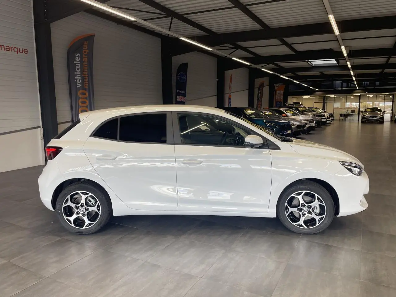 Vue de profil côté gauche d’une MG3 1.5 Hybrid+ blanche avec jantes alliage 16 pouces en showroom.