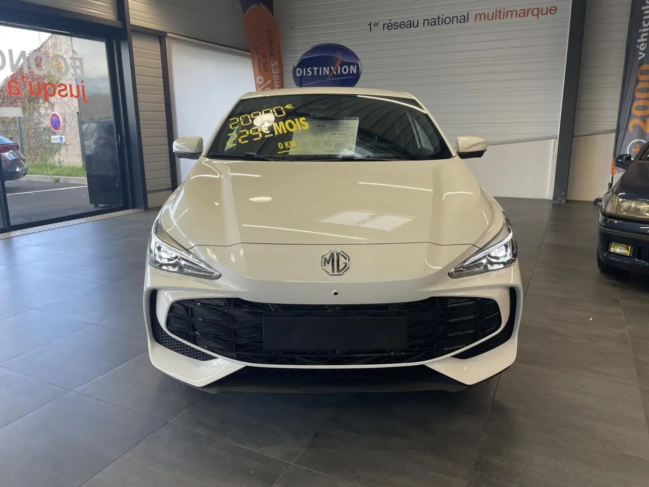 Vue avant d'une MG3 1.5 Hybrid+ blanche avec calandre noire et phares LED allumés en showroom.