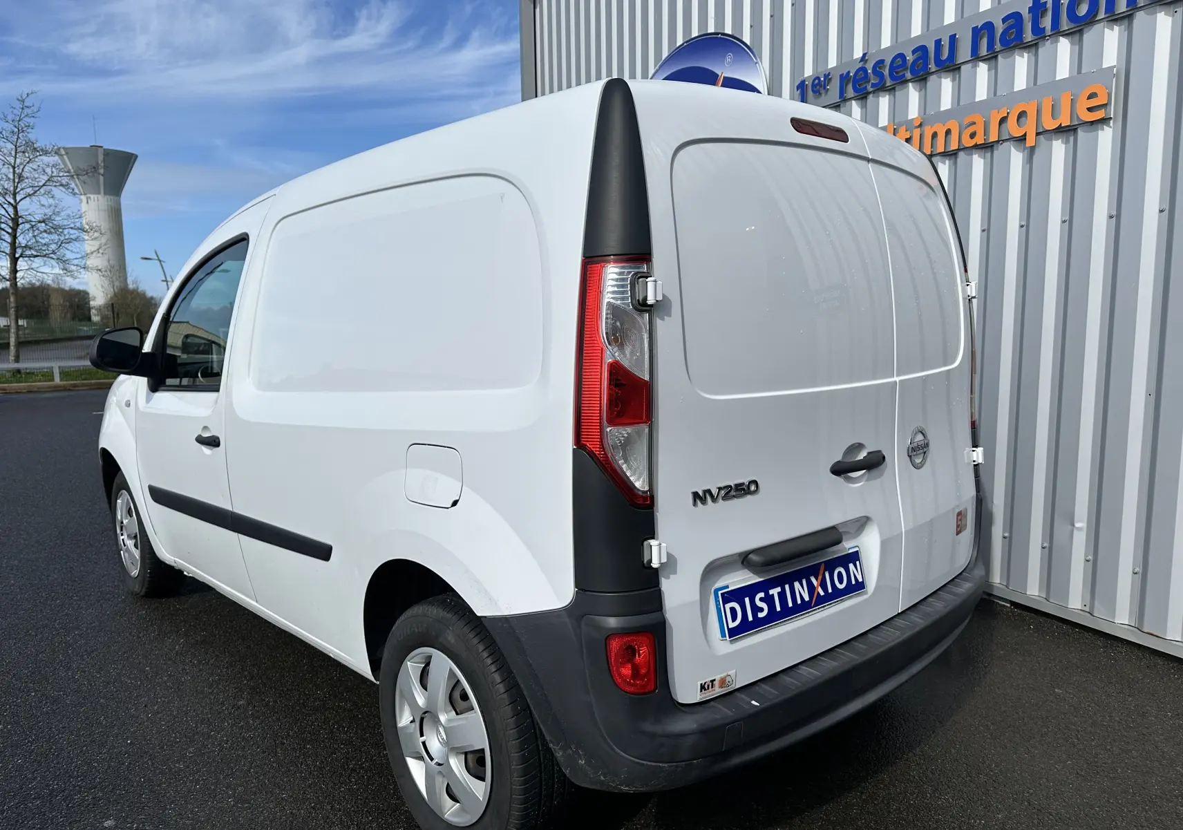 Vue 3/4 arrière droite d'un utilitaire Nissan NV250 blanc de 2020 avec logo et plaque Distinxion visible.