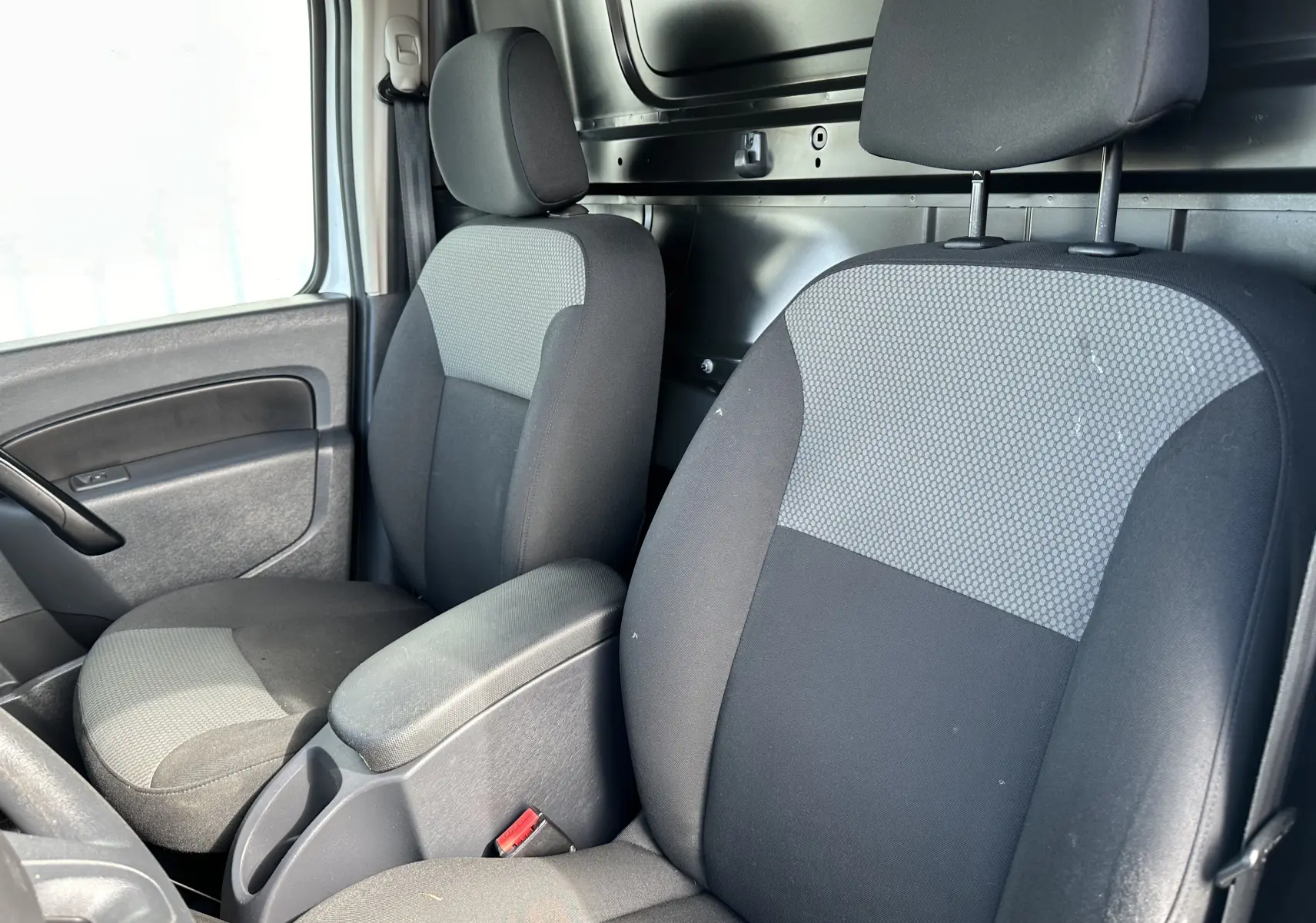 Vue intérieure du Nissan NV250 1.5 DCI 95 Optima 2020 montrant les sièges avant noirs avec appuie-têtes et accoudoir central.