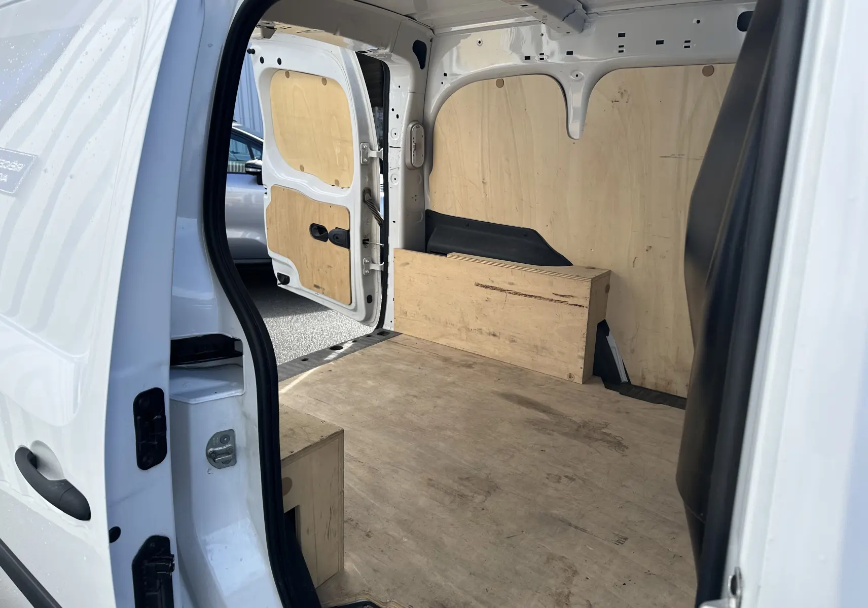 Vue intérieure arrière du fourgon utilitaire Nissan NV250 blanc de 2020, avec aménagement bois dans l'espace de chargement.