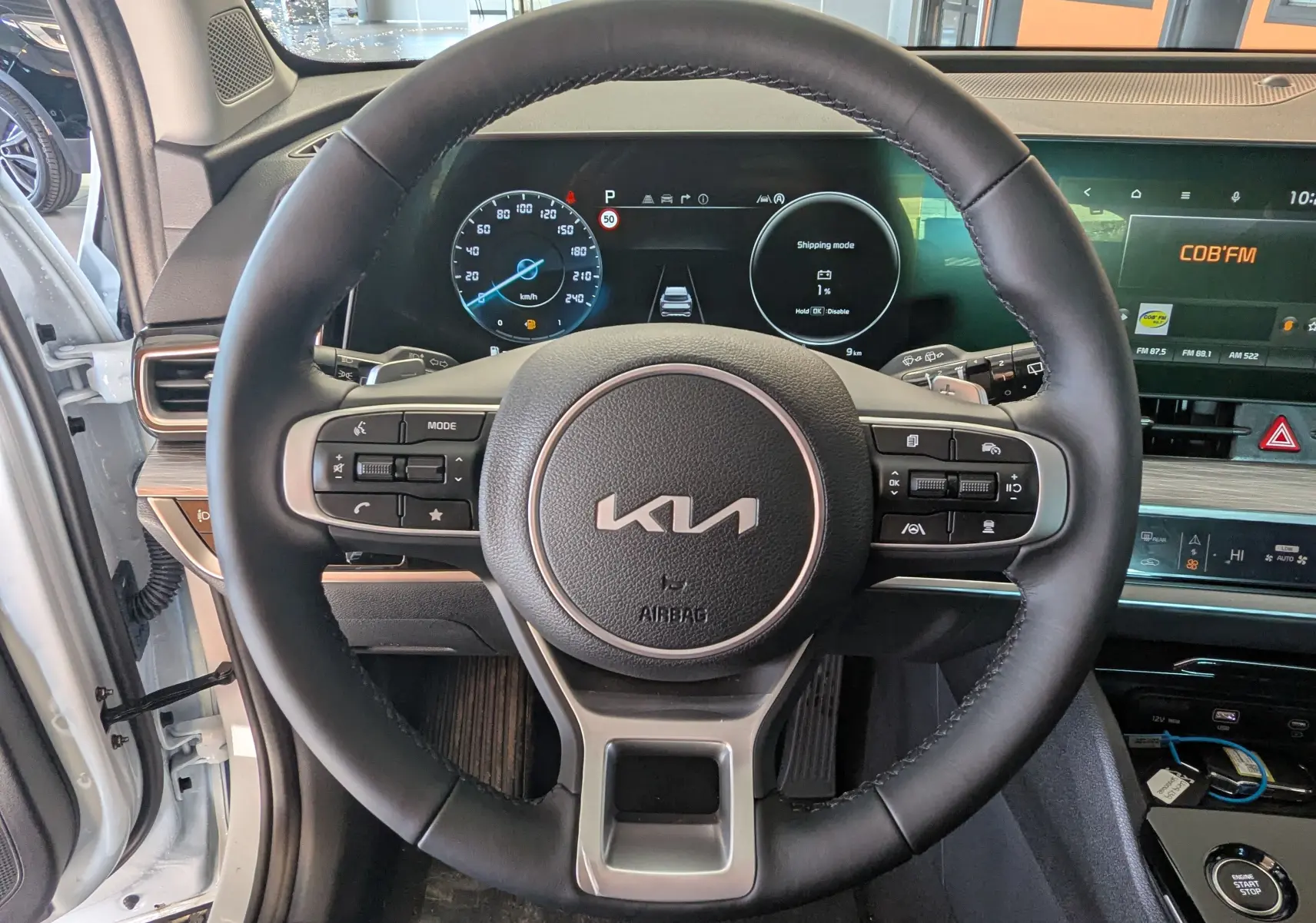 Vue rapprochée du volant cuir noir du Kia Sportage blanc MY25 avec tableau de bord digital et écran tactile.