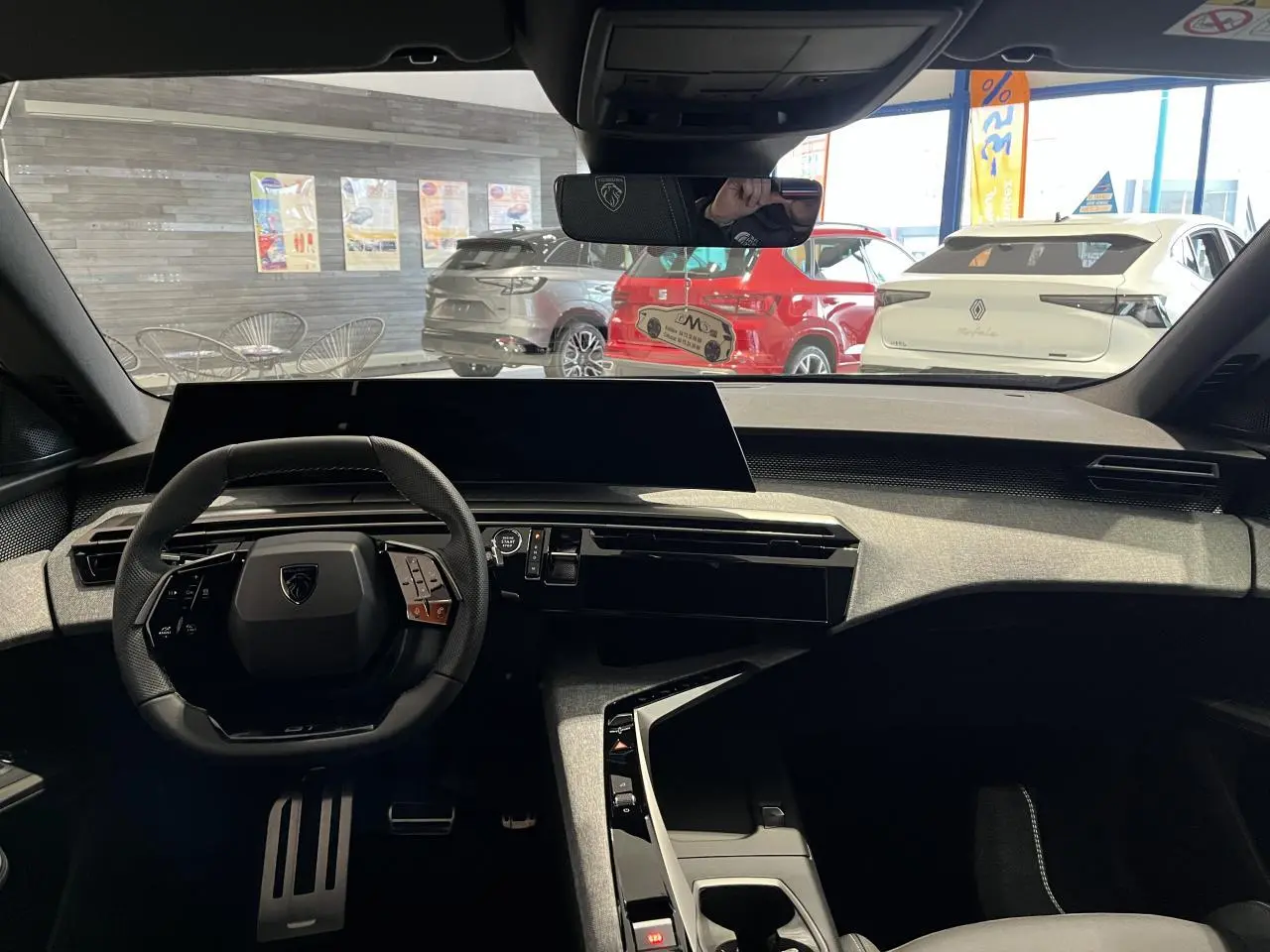 Vue intérieure avant du Peugeot 3008 gris titanium 2025, avec tableau de bord moderne et volant compact noir.