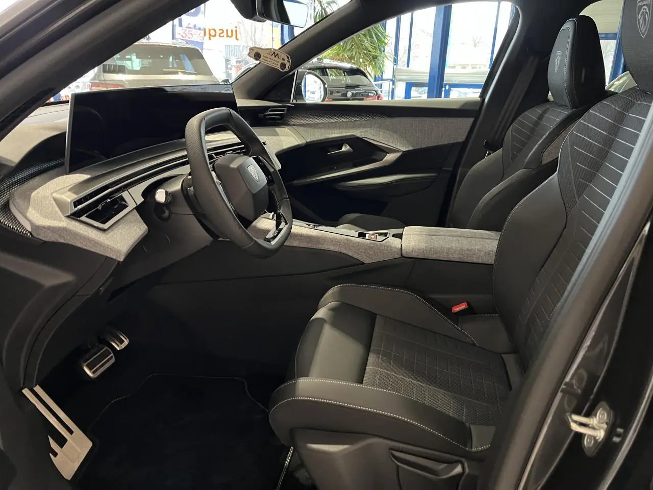 Vue intérieure côté conducteur du Peugeot 3008 gris titanium 2025, avec sièges tissu et volant compact noir laqué.