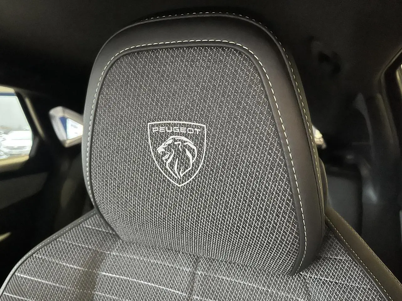 Gros plan sur l'appuie-tête avant avec logo Peugeot brodé sur tissu gris chiné, intérieur noir du 3008 GT 2025.