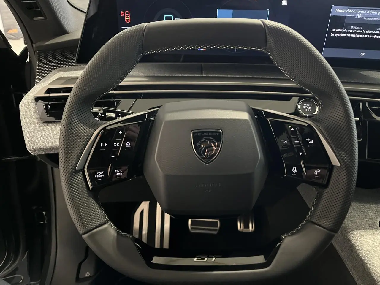 Volant compact noir laqué avec badge Peugeot et inscription GT, vue frontale de l'intérieur du Peugeot 3008 gris titanium.