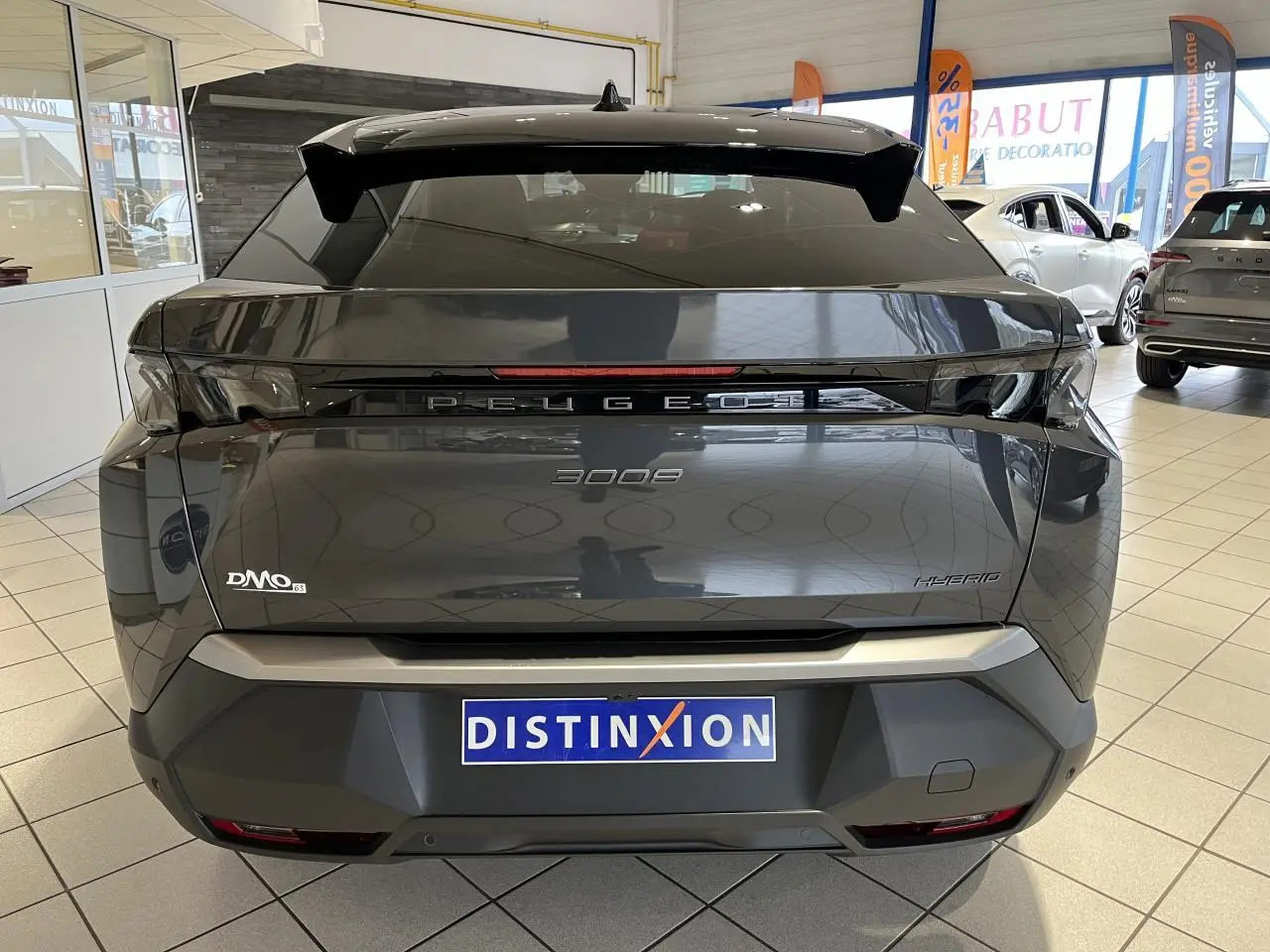 Vue arrière d'un Peugeot 3008 gris titanium hybride, avec bandeau noir laqué entre feux et logo Peugeot visible.