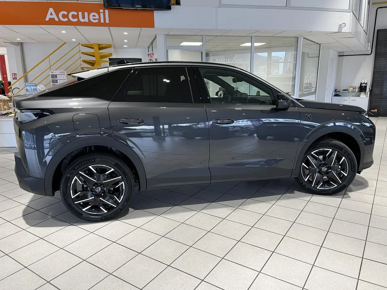 Profil droit du Peugeot 3008 GT hybride gris titanium en showroom, avec jantes alliage 19 pouces et vitres teintées.