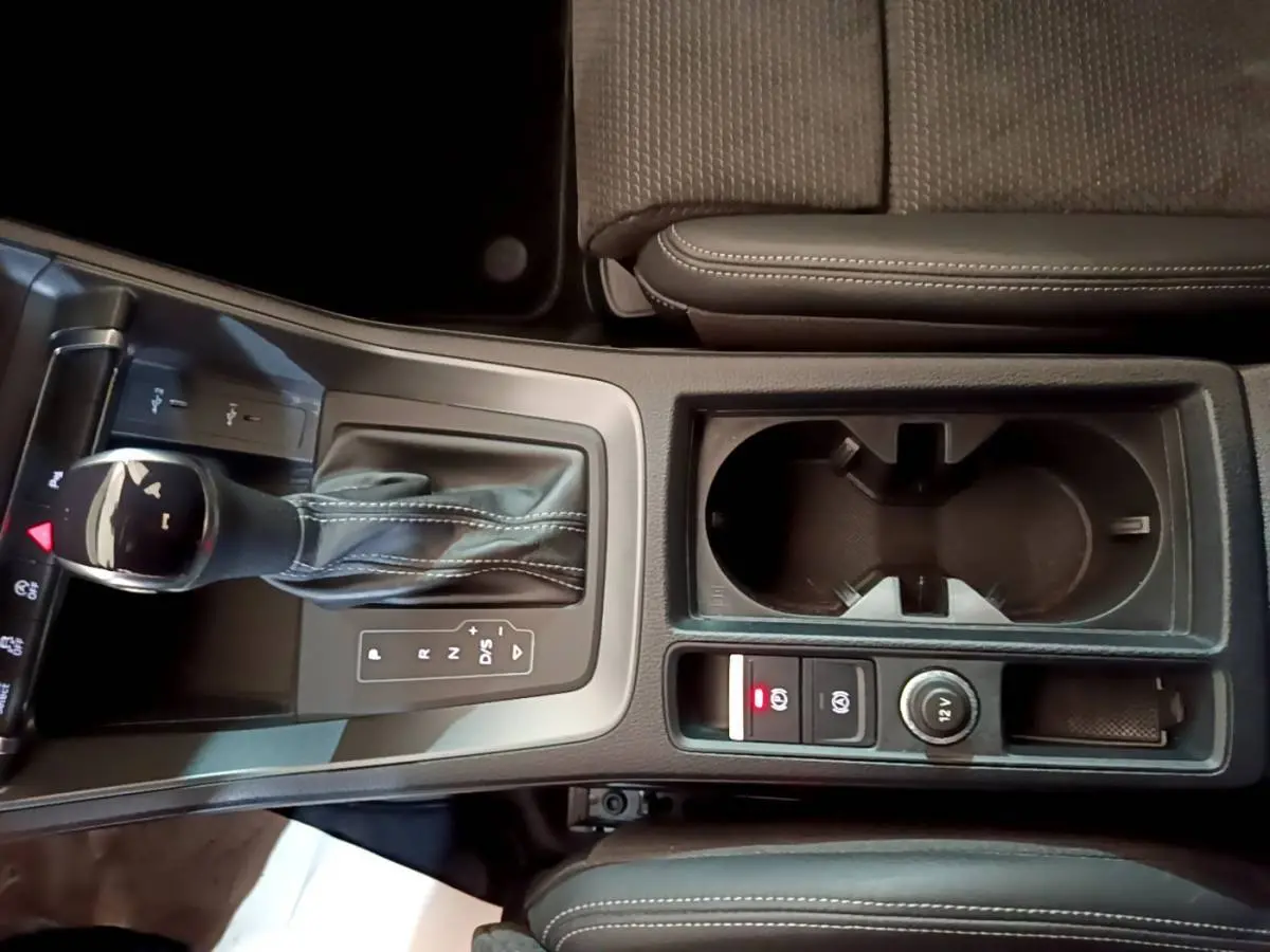 Vue plongeante sur la console centrale noire de l'Audi Q3 35 TFSI S Line avec levier de vitesse automatique et porte-gobelets.