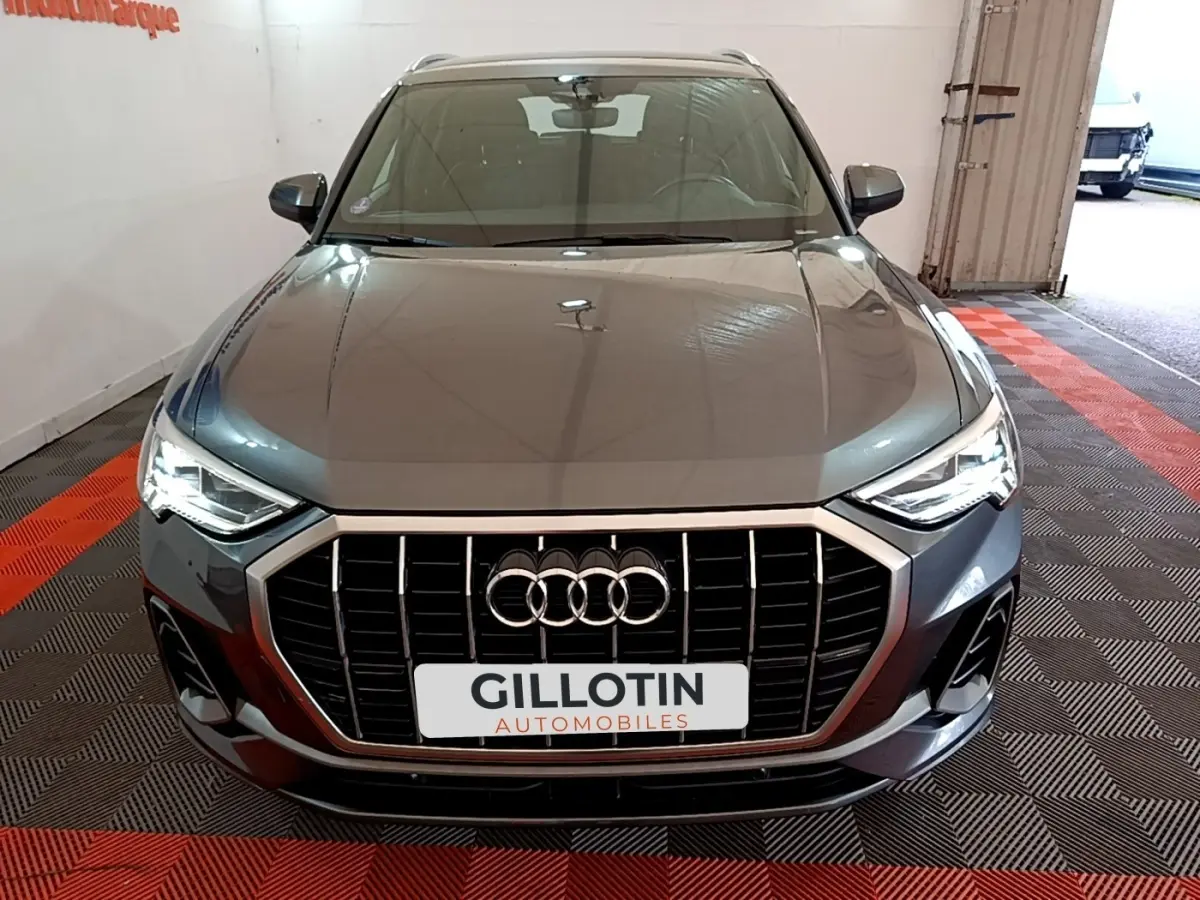 Vue avant d'un Audi Q3 gris foncé 35 TFSI S Line 2022 avec calandre large et phares LED allumés.