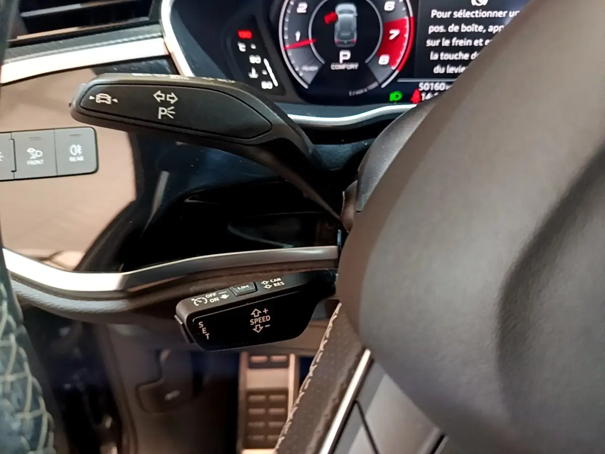Gros plan sur la commande de régulateur de vitesse et clignotants du volant cuir noir de l'Audi Q3 gris foncé 2022.