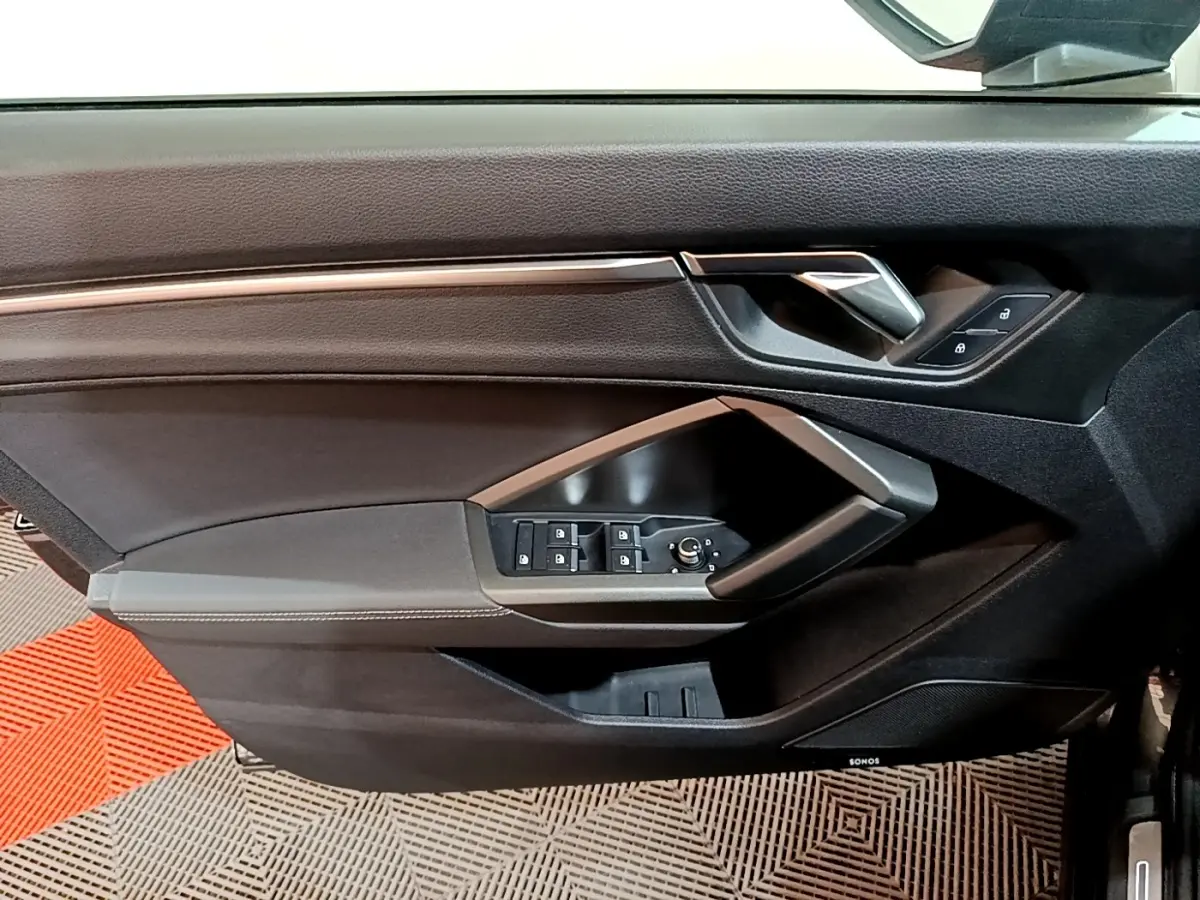 Gros plan sur la porte côté gauche de l'Audi Q3 gris foncé, avec commandes de vitres et poignée argentée.