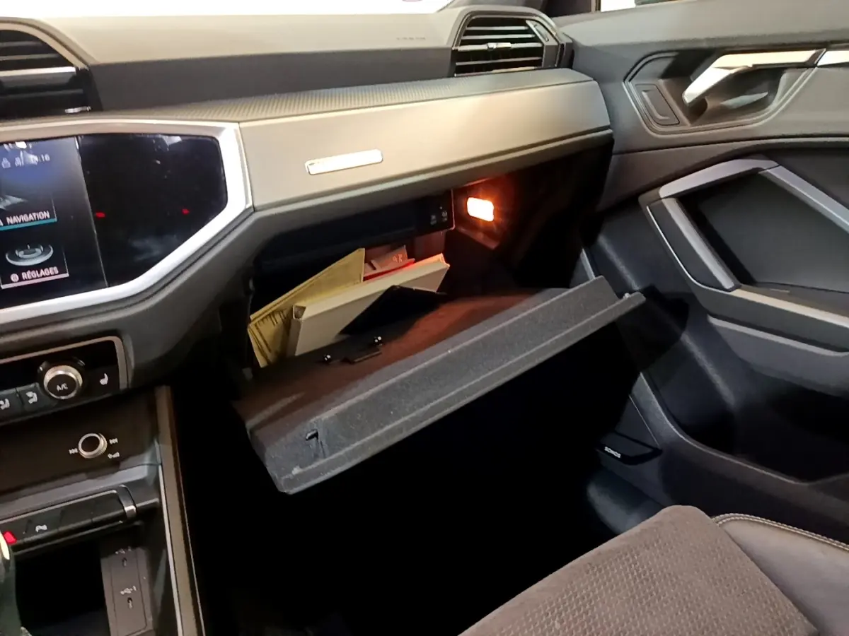 Intérieur de l’Audi Q3 35 TFSI S Line 2022, vue côté passager avec boîte à gants ouverte et tableau de bord gris foncé.