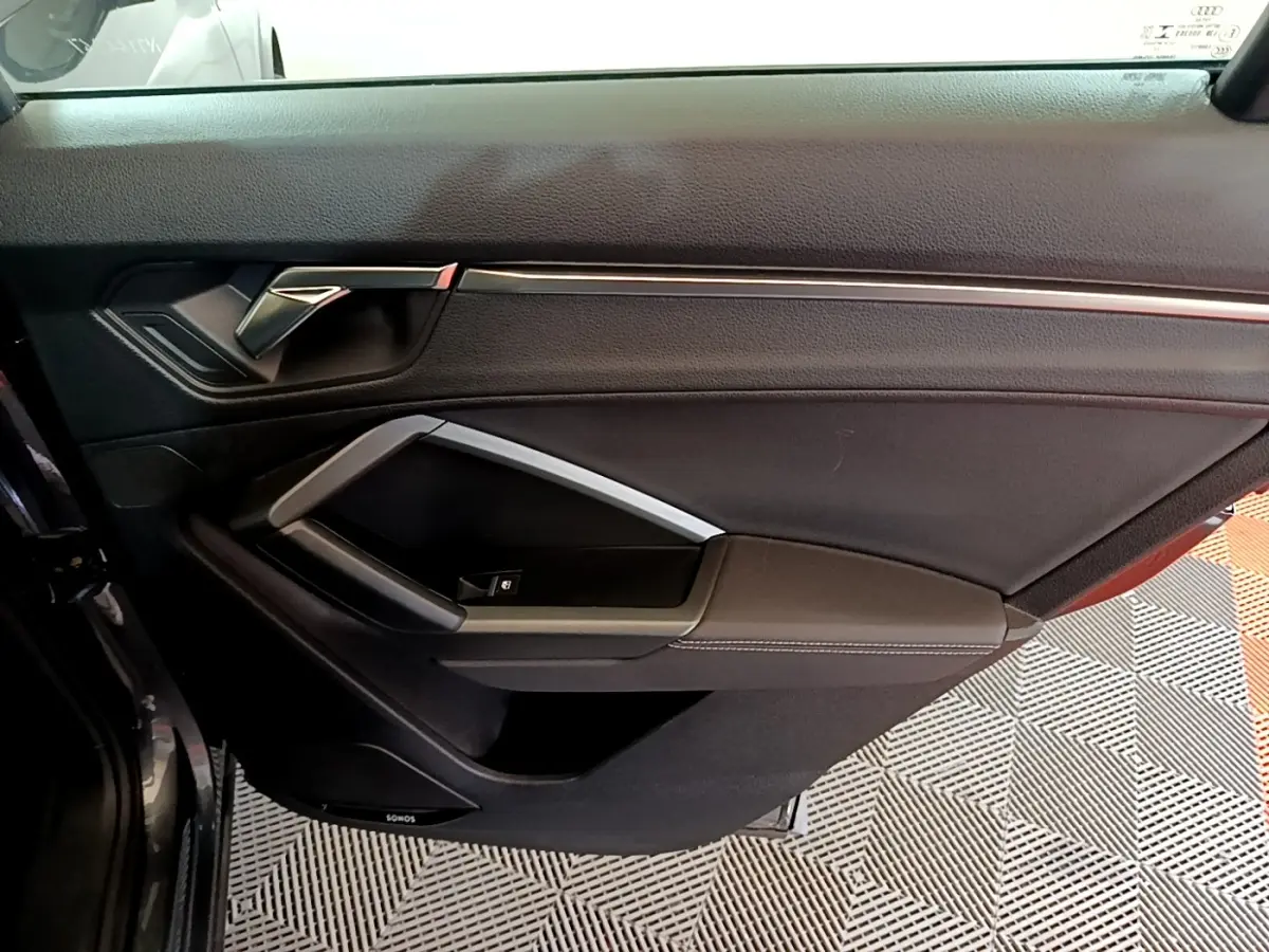 Détail de la porte intérieure côté gauche de l'Audi Q3 gris foncé avec poignée argentée et commande de vitre.