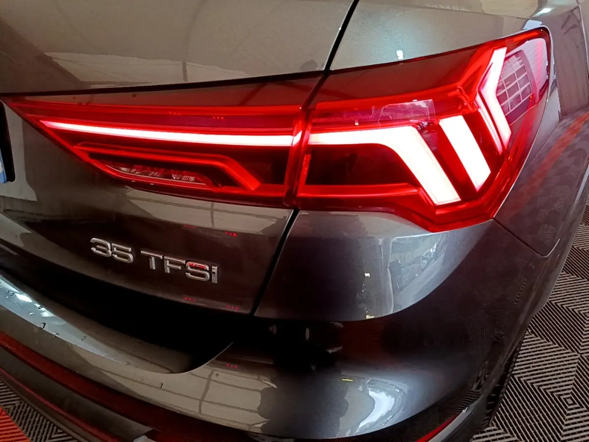 Gros plan sur le feu arrière droit rouge et le badge 35 TFSI d’un Audi Q3 gris foncé 2022.