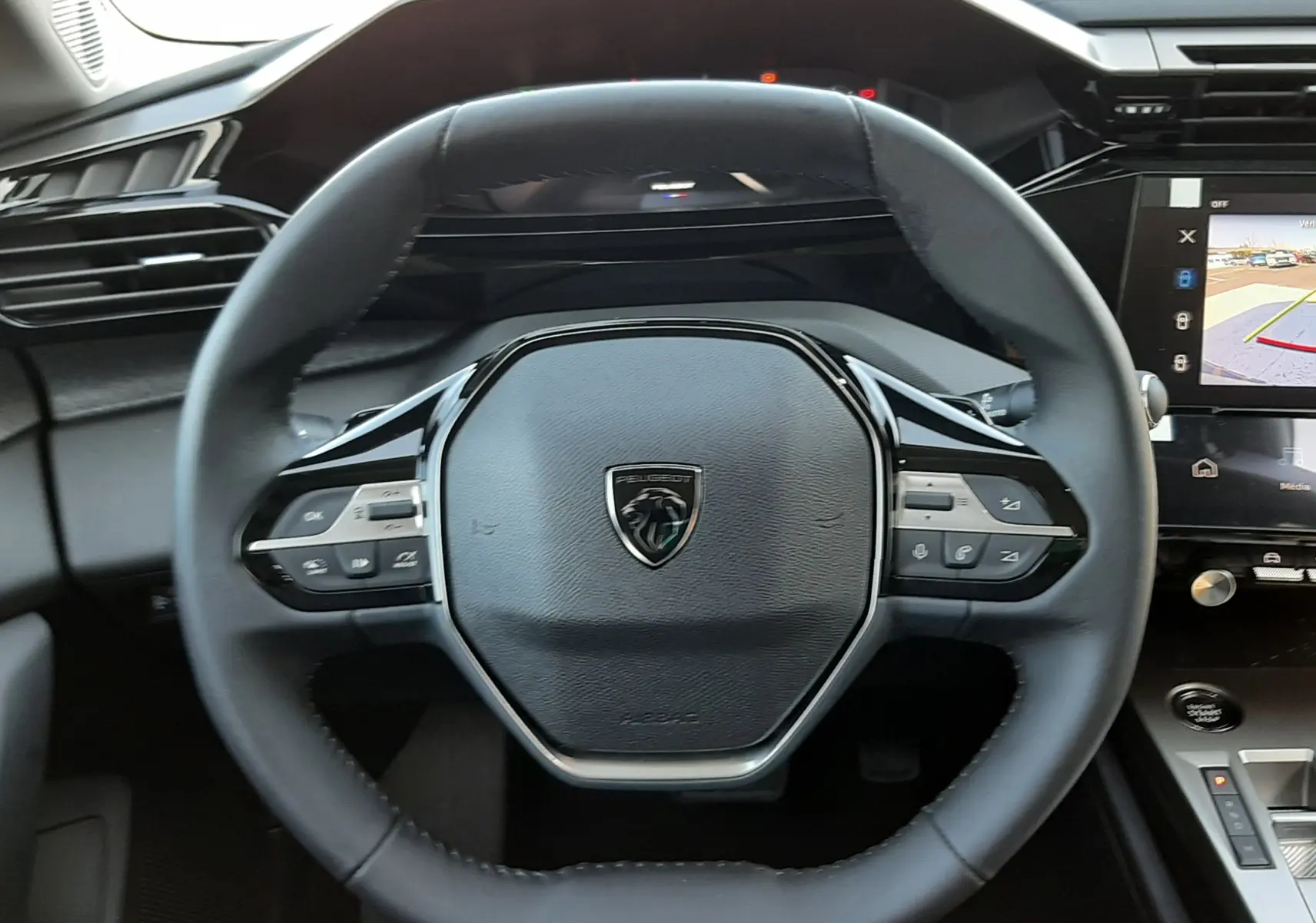 Vue rapprochée du volant multifonction noir de la Peugeot 308 2026 avec tableau de bord digital et écran central affichant la caméra 360°.