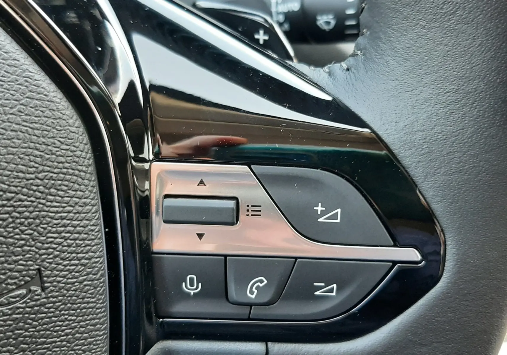 Gros plan sur les commandes multifonctions noires à gauche du volant en cuir d'une Peugeot 308 2026.