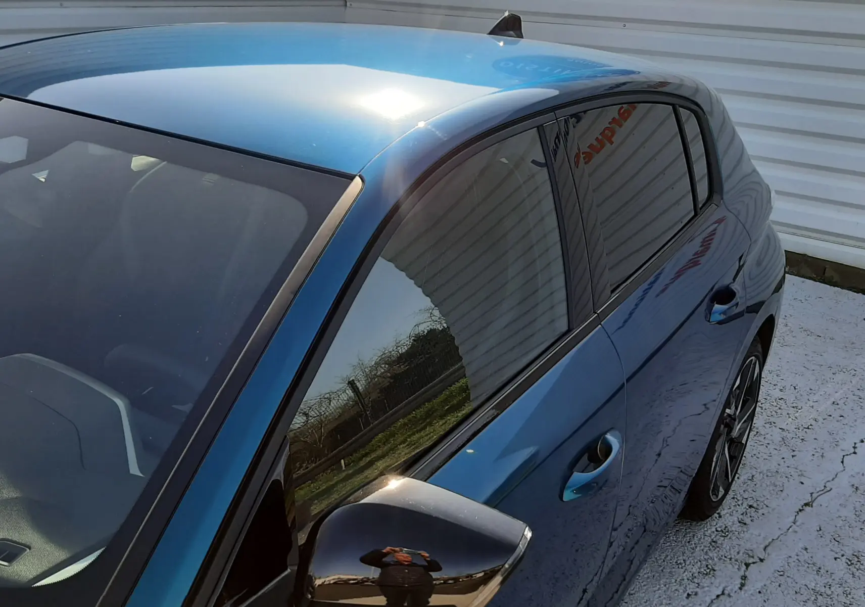 Vue 3/4 avant droit d'une Peugeot 308 Bleu Obsession avec rétroviseur noir brillant et vitres teintées.