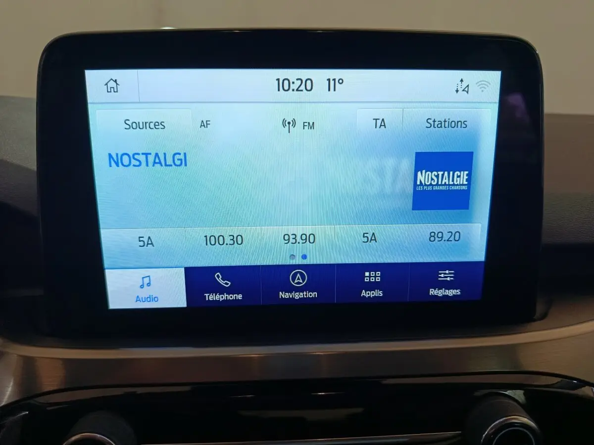 Écran tactile central affichant la radio Nostalgie dans l'habitacle du Ford Kuga gris foncé, vue de face.
