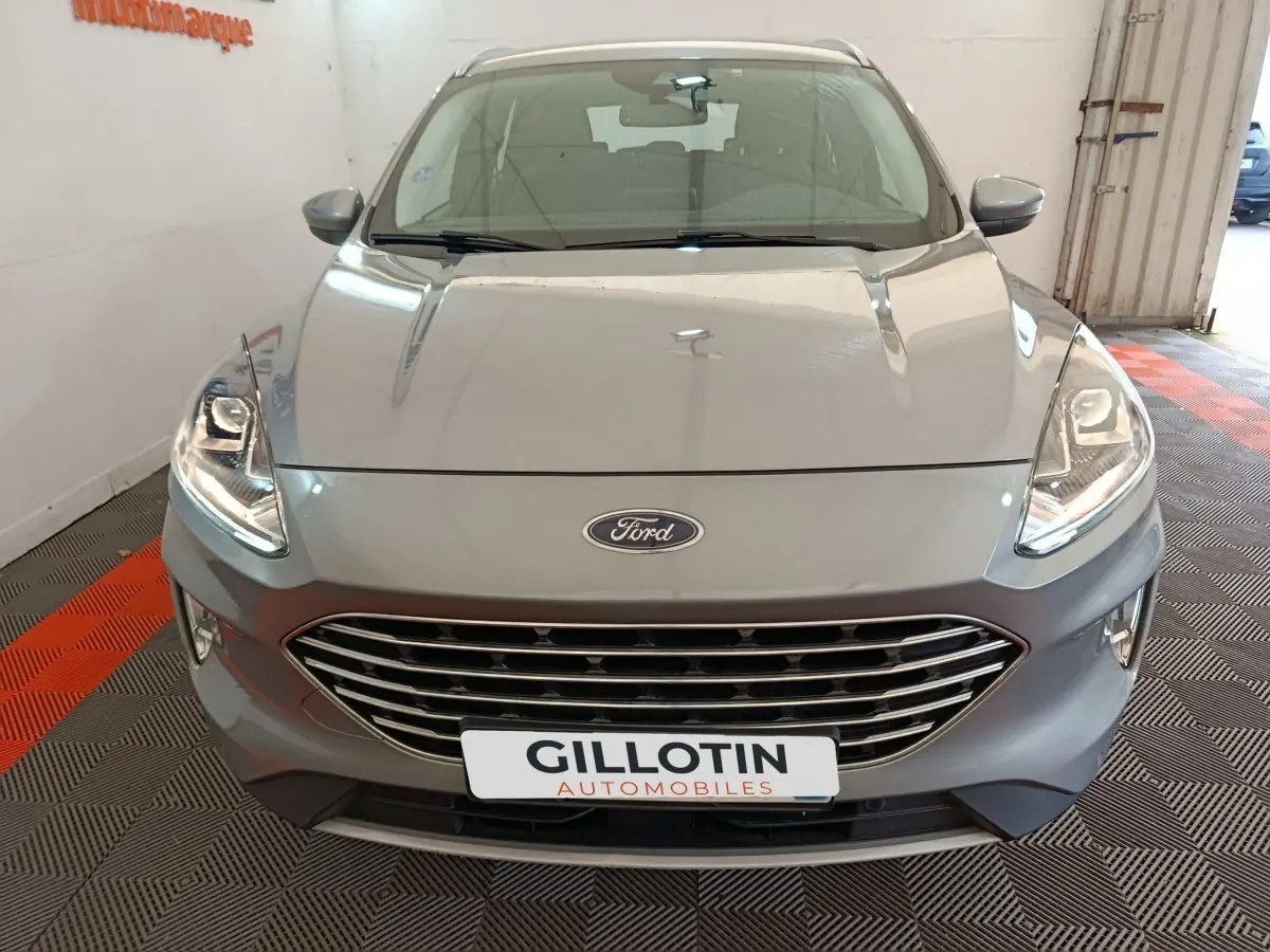 Vue avant d'un Ford Kuga gris foncé 2023 avec calandre chromée et phares LED allumés en intérieur showroom.