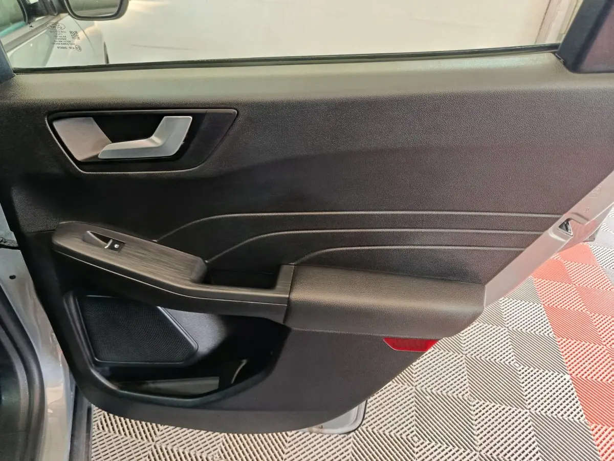 Vue intérieure de la porte avant gauche du Ford Kuga gris foncé, avec poignée argentée et commande de vitre.