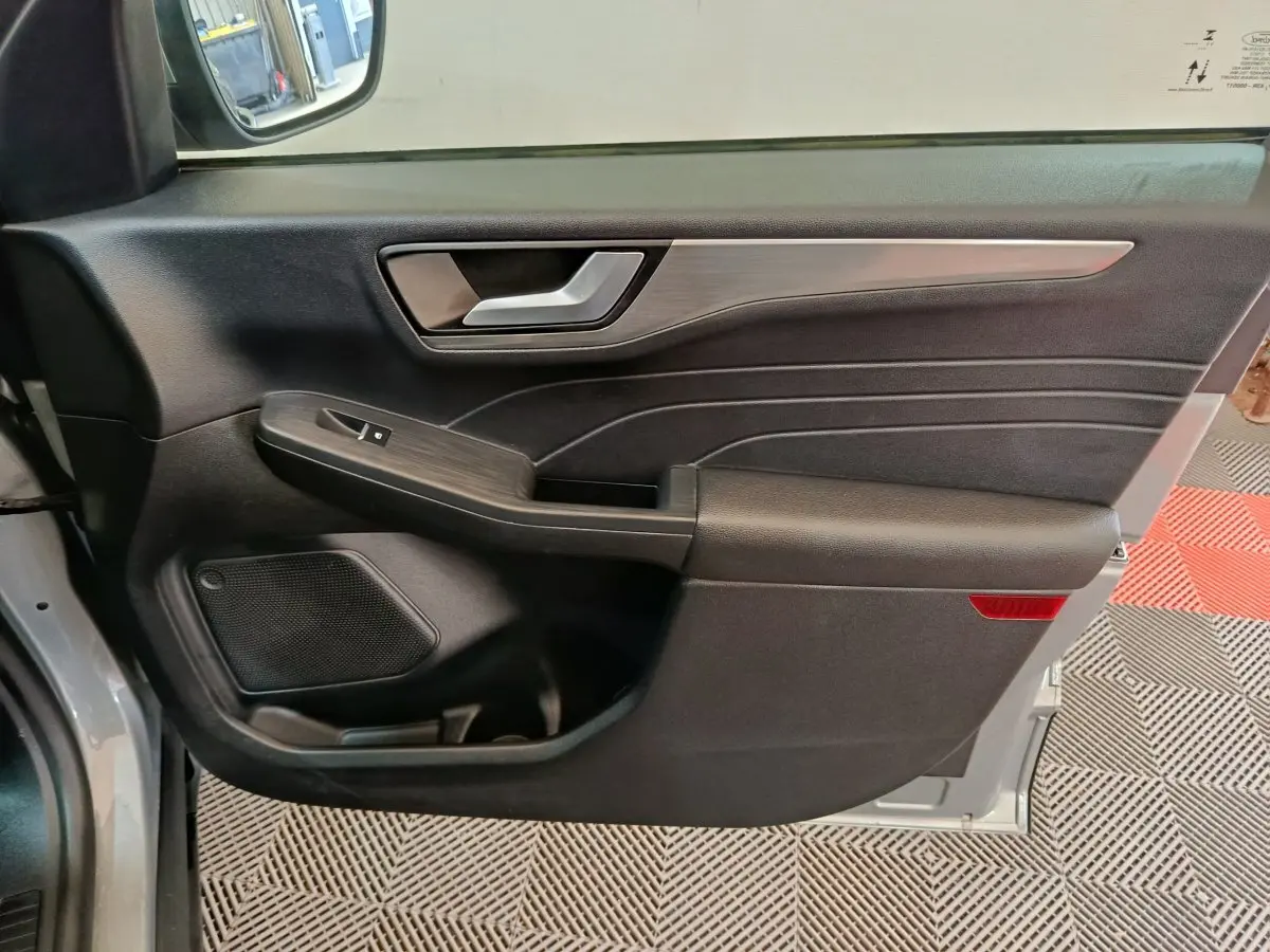 Vue intérieure côté gauche de la porte avant d’un Ford Kuga gris foncé avec garniture noire et insert décoratif métallique.
