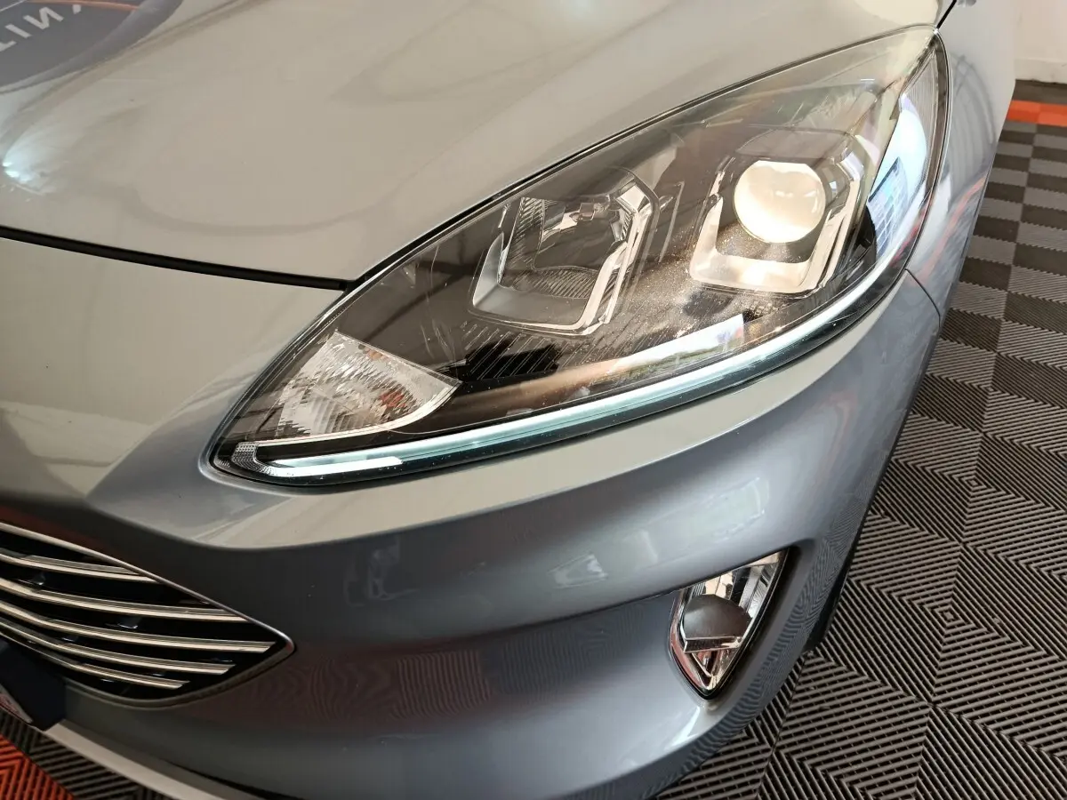 Gros plan sur le phare avant droit et la calandre d’un Ford Kuga gris foncé 2023, avec antibrouillards intégrés.