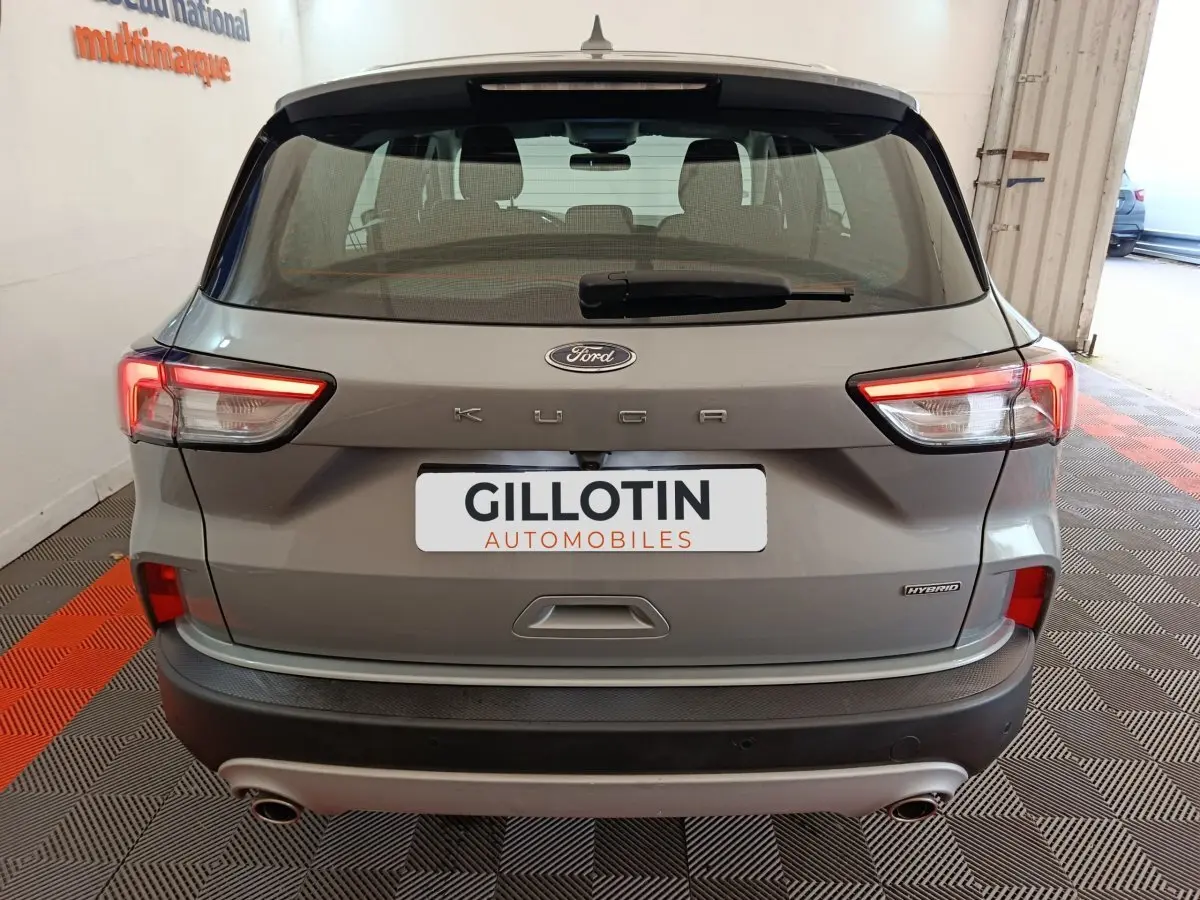 Vue arrière d’un Ford Kuga gris foncé hybride 2023 avec feux LED allumés et double sortie d’échappement visible.
