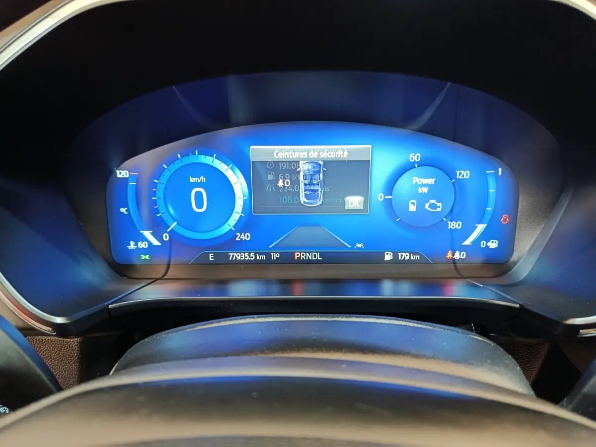 Vue rapprochée du combiné d'instruments numérique bleu du Ford Kuga 2023, affichant la vitesse et alertes de sécurité.