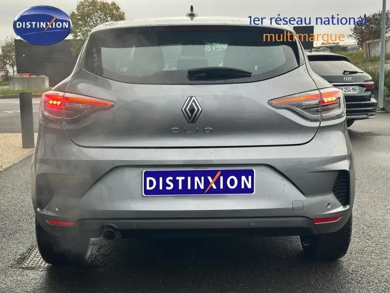 Vue arrière d'une Renault Clio grise 2025 avec feux allumés et logo distinctif au centre du hayon.