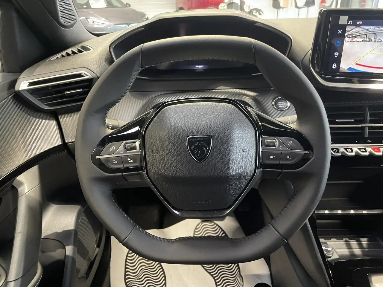 Vue intérieure centrée sur le volant compact noir du Peugeot 2008 1.2i Hybrid 2026 avec tableau de bord carbone.